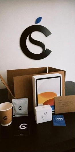Caixa de entrega da Cescho com iPad, AirPods, copo, café e voucher