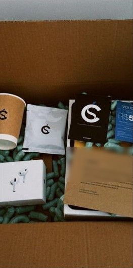 Caixa da Cescho aberta com AirPods, café, carta e voucher